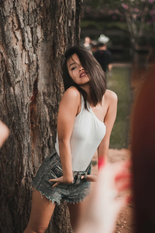 a woman leaning against a tree in a park, by Robbie Trevino, wearing white camisole, instagram model, malaysian, 5 0 0 px models