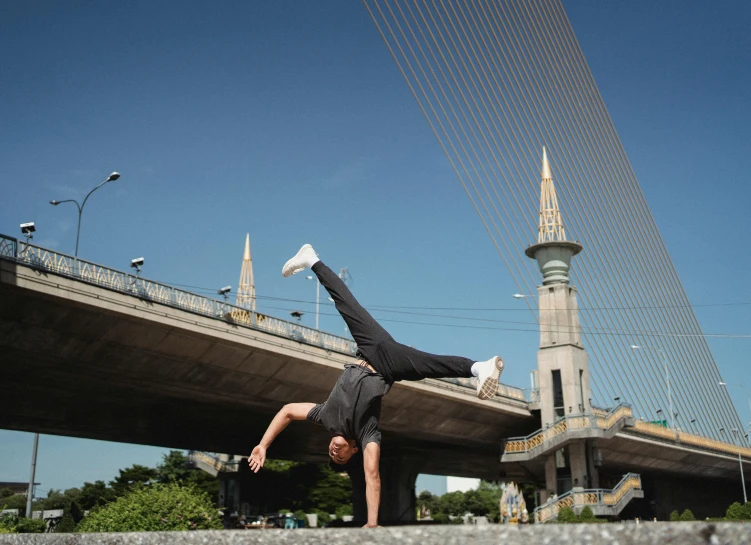 a man doing a handstand in front of a bridge, arabesque, riyahd cassiem, mark brookes, in the middle of the city, profile image