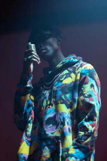 a man standing on top of a stage holding a microphone, an album cover, pexels, visual art, young thug, wearing shades, patterned clothing, contemplating