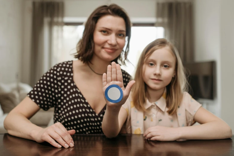 a woman and a little girl sitting at a table, by Adam Marczyński, pexels contest winner, interactive art, huge magic circles on the hand, sitting on a red button, light sensor, 3 d print