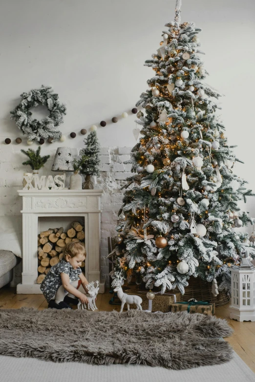 a little boy sitting in front of a christmas tree, lots of decoration and furniture, white and grey, woodland location, home display