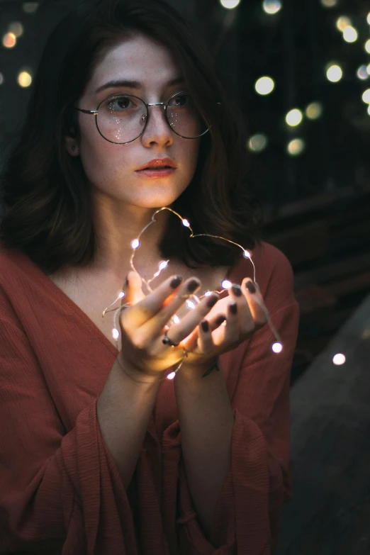 a woman holding a string of lights in her hands, pexels contest winner, girl wearing round glasses, thoughtful ), lofi, uncropped