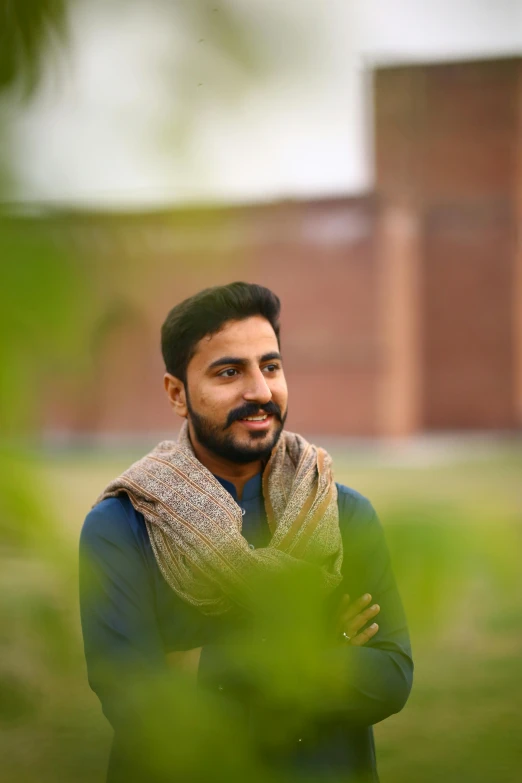 a man standing in front of a building wearing a scarf, a picture, by Manjit Bawa, academic art, portrait shot 8 k, trees in background, ((portrait)), with mustache