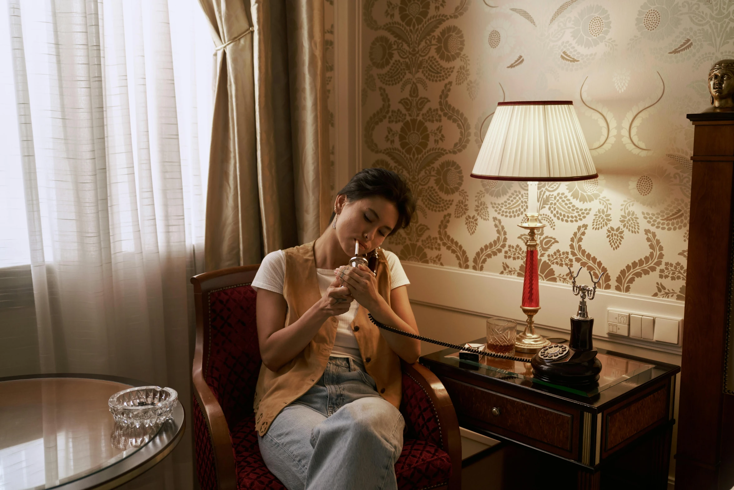 a woman sitting in a chair next to a lamp, drinking a glass of whiskey, paris hotel style, louise zhang, glass and gold pipes