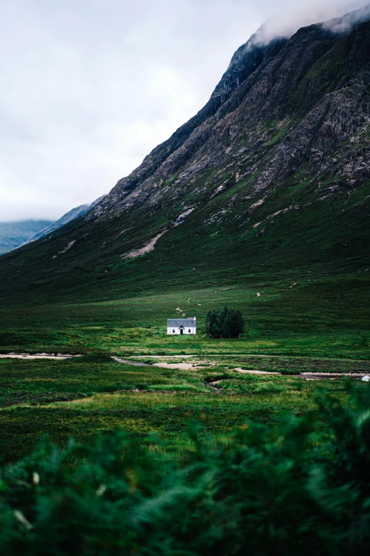 a small white house sitting on top of a lush green field, inspired by Elsa Bleda, unsplash contest winner, scottish highlands, moody colors, 2000s photo, mountainous