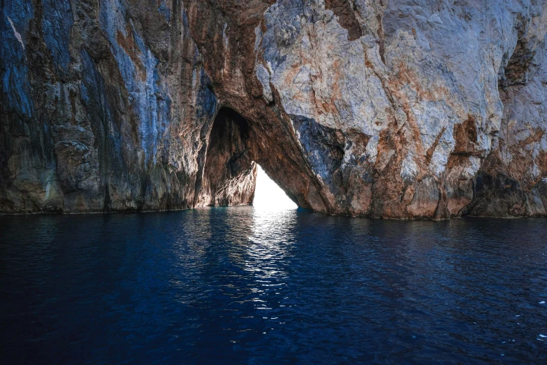 a cave in the middle of a body of water, dark blue water, piroca, with the sun shining on it, pareidolia