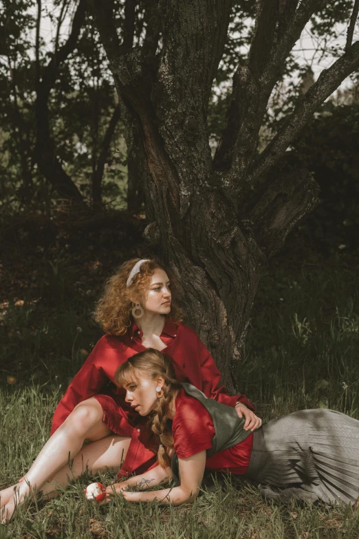 a couple of women sitting on top of a lush green field, an album cover, unsplash, renaissance, red curled hair, red clothes, on a tree, 5 0 0 px models