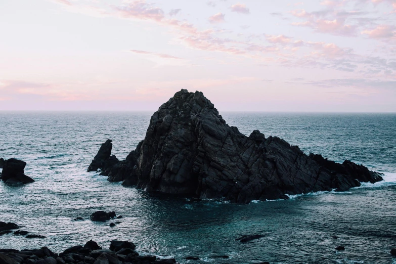 a large rock in the middle of a body of water, by Lee Loughridge, unsplash contest winner, minimalism, hills and ocean, devils horns, early evening, victoria siemer