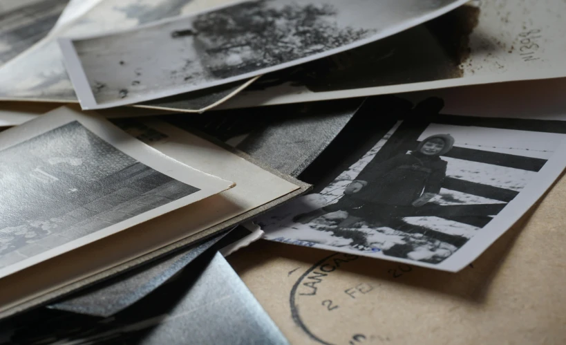 a pile of old photos sitting on top of a table, a black and white photo, unsplash, process art, cardboards ; mess, promo image, ww1 photo, high angle close up shot