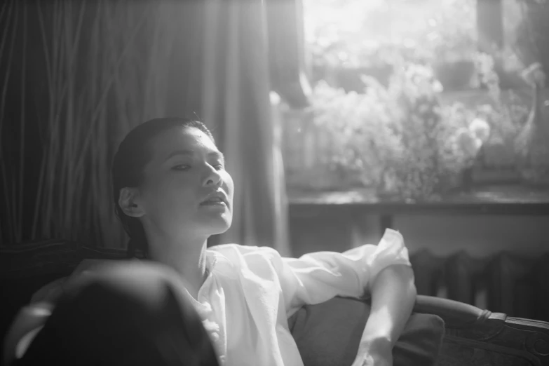 a woman sitting on a couch with her eyes closed, a black and white photo, by Maurycy Gottlieb, maggie cheung, summer morning light, clothed in white shirt, aleksander rostov