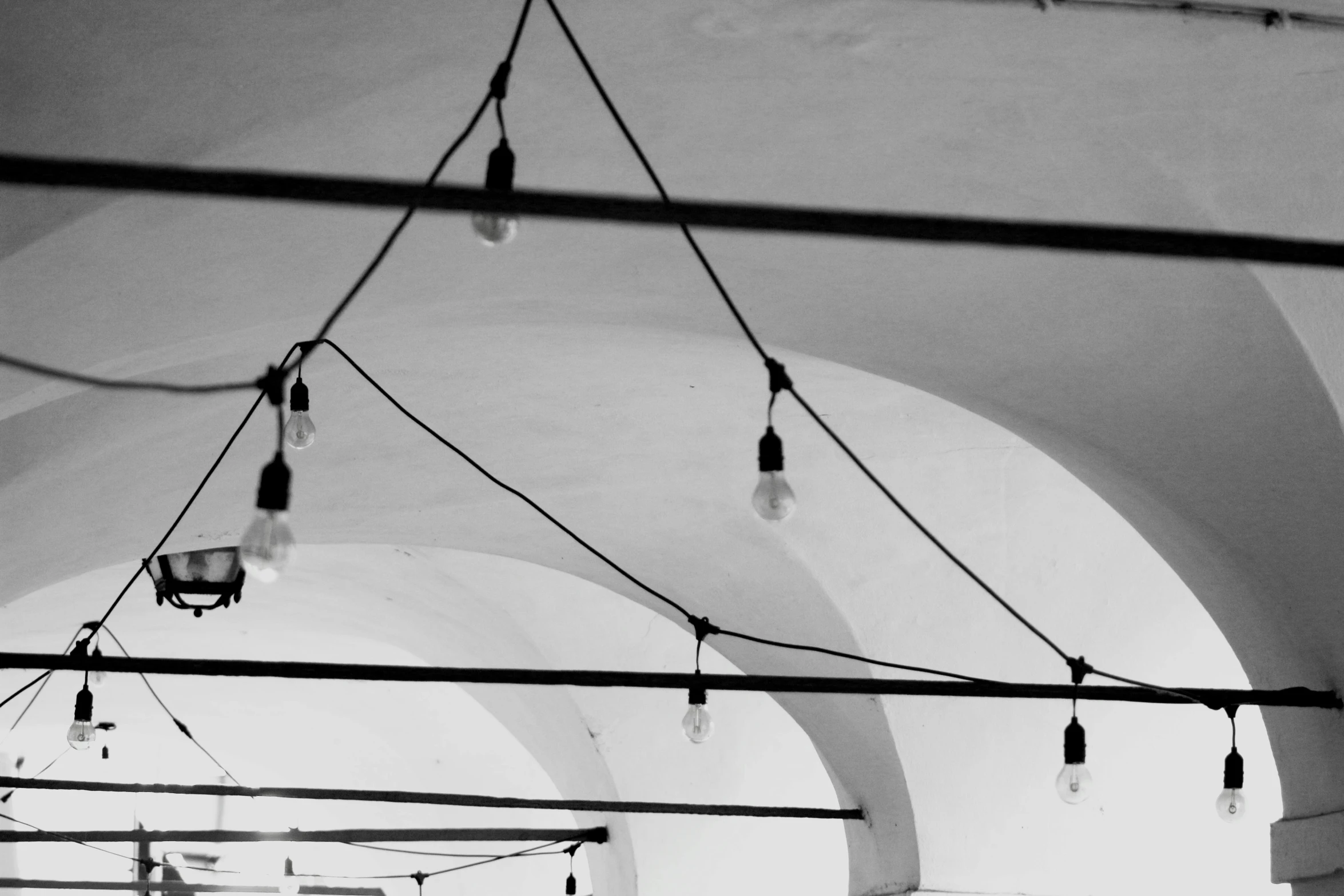 a black and white photo of the inside of a building, by Emma Andijewska, unsplash, string lights, arched ceiling, white walls, lamps