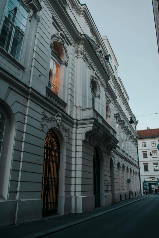 a double decker bus driving down a street next to tall buildings, danube school, neoclassical architecture, many doorways, in the evening, austrian architecture