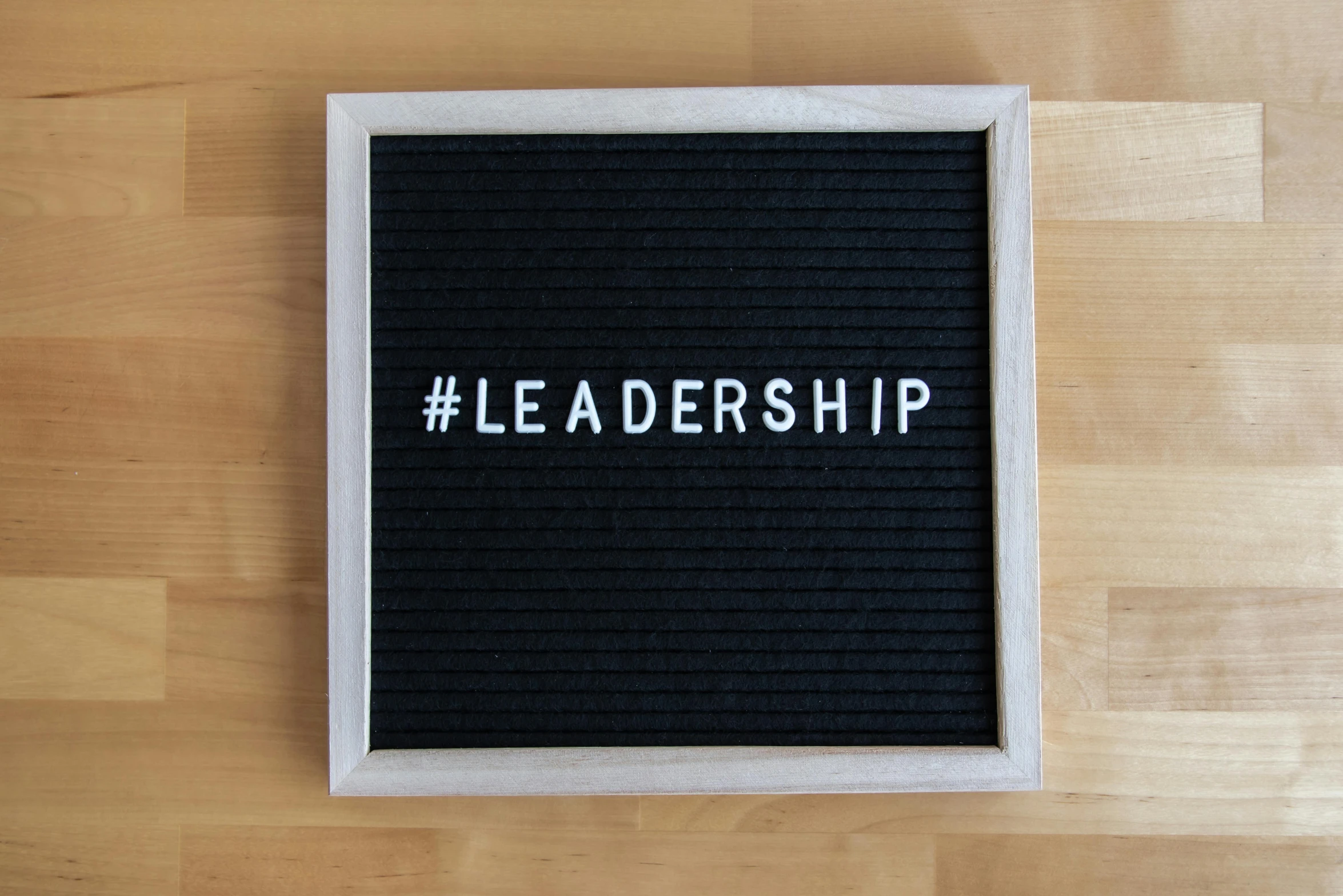 a black letter board sitting on top of a wooden floor, by Emma Andijewska, trending on unsplash, letterism, strong leader, 1 6 x 1 6, leathery, teams