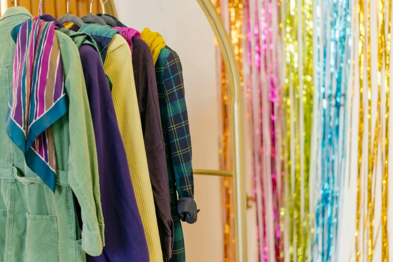 a rack of colorful shirts hanging on a wall, by Helen Stevenson, trending on unsplash, gold green blue purple, streamers, wearing festive clothing, a wide shot