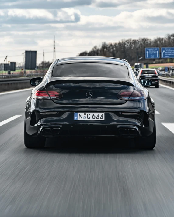 a car driving down a highway on a cloudy day, by Adam Marczyński, pexels contest winner, mercedez benz, back pose, black on black, on a street race track