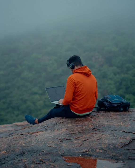 a man sitting on a rock with a laptop, trending on pexels, overcast weather, with head phones, view from the top, lgbtq