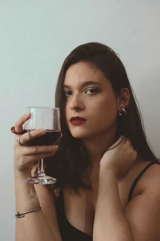 a woman holding a wine glass in front of her face, a portrait, inspired by Elsa Bleda, pexels contest winner, renaissance, she is wearing a black tank top, dark lipstick, androgynous person, girl with dark brown hair