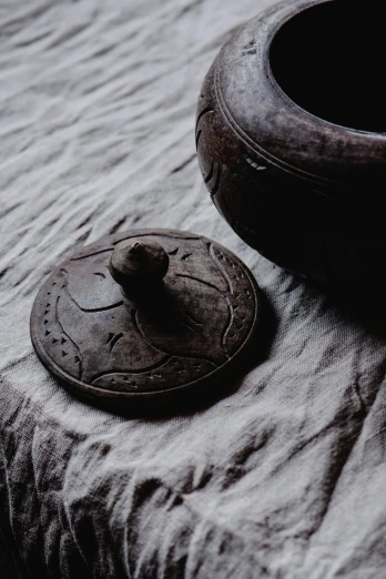 a wooden bowl sitting on top of a table, an album cover, inspired by Gong Kai, unsplash, visual art, stone carving, dark grey, hyperdetailed scp artifact jar, tuareg
