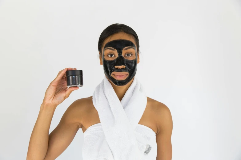 a woman holding a black mask in front of her face, textured base ; product photos, black oil bath, with a white complexion, black female