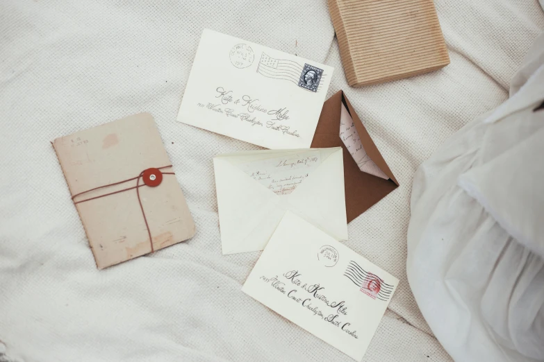 a couple of envelopes sitting on top of a bed, by Carey Morris, pexels contest winner, letterism, silver，ivory, rubber stamp, brown, thumbnail