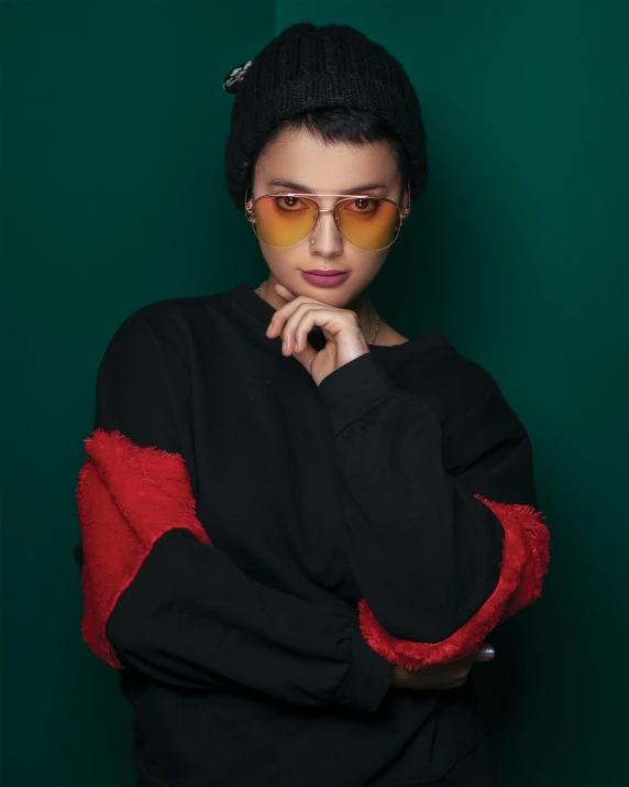 a woman standing in front of a green wall, an album cover, inspired by Elsa Bleda, trending on pexels, antipodeans, black sweater, wearing red tainted glasses, gradient red to yellow, portrait androgynous girl