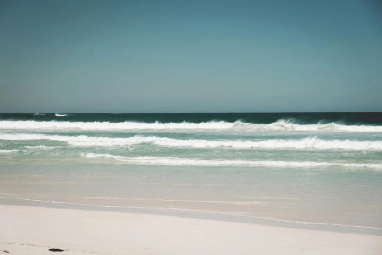 a man standing on top of a beach next to the ocean, unsplash contest winner, minimalism, the emerald coast, foamy waves, south african coast, sparsely populated