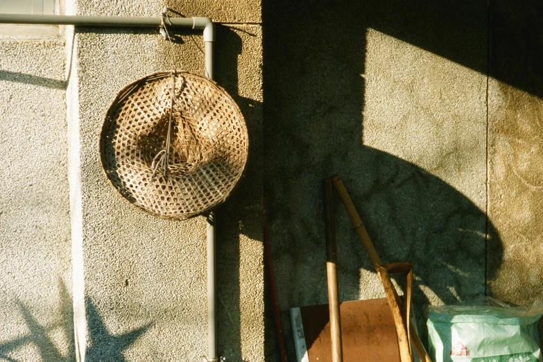 a hat hanging on the side of a building, by Elsa Bleda, shin hanga, afternoon sunlight, chengwei pan, 90s photo, wicker art