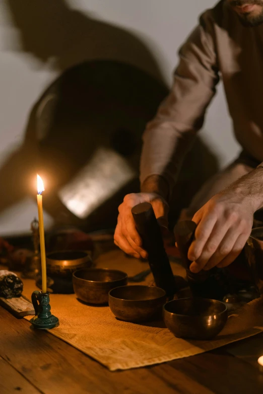 a man lighting a candle on a wooden table, pexels contest winner, renaissance, mortar and pestle, bells, black, promo image