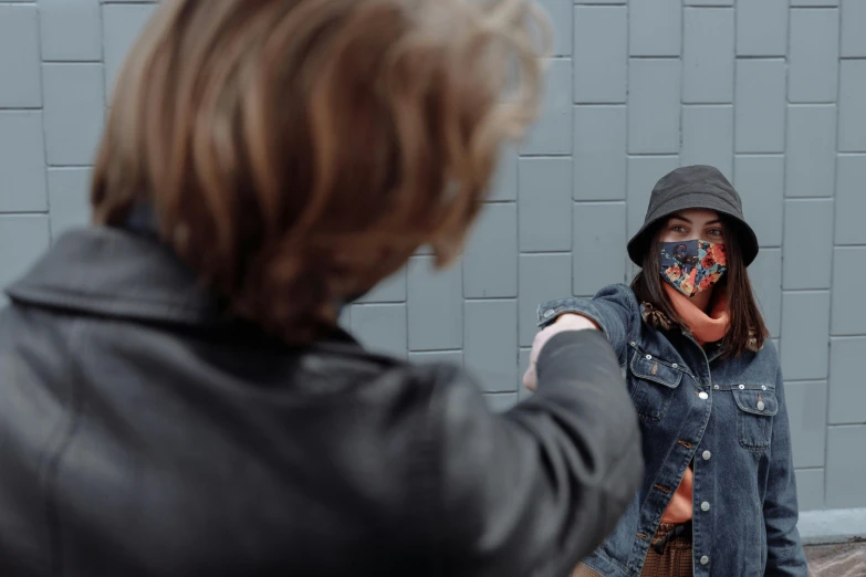 a woman standing next to a man wearing a face mask, by Emma Andijewska, pexels contest winner, graffiti, meet the actor behind the scenes, hands shielding face, wearing a jeans jackets, people fighting