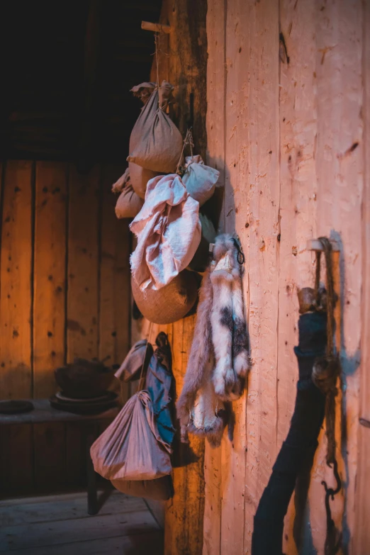 a couple of bags hanging from the side of a wall, a still life, by Jan Tengnagel, trending on unsplash, renaissance, inside primitive hut, real fur and real skin, at twilight, ( ( photograph ) )
