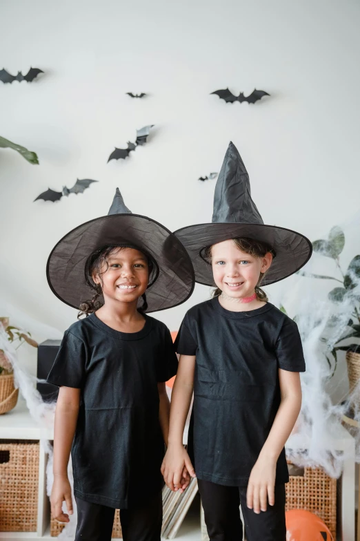 two children in halloween costumes standing next to each other, pexels contest winner, black pointed hat, indoor picture, promotional image, petite