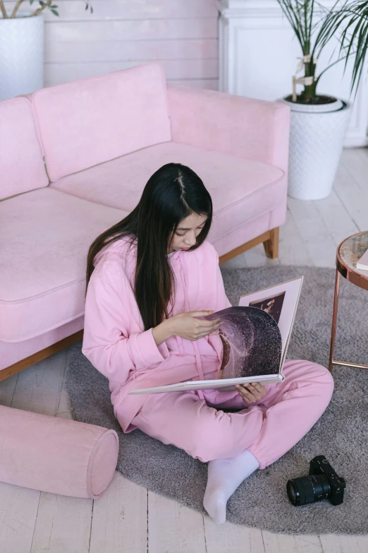 a woman sitting on the floor using a laptop, a picture, inspired by Ruth Jên, pexels contest winner, wearing a pastel pink hoodie, reading nook, wearing human air force jumpsuit, gif