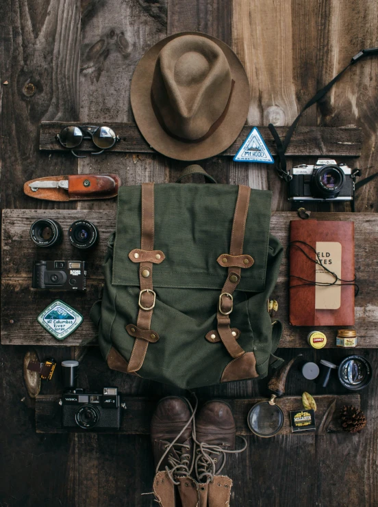 a hat, camera, camera case and other items laid out on a wooden surface, inspired by Wes Anderson, trending on unsplash, renaissance, square backpack, ( ( dark green, detail shot, full - body portrait of a ranger