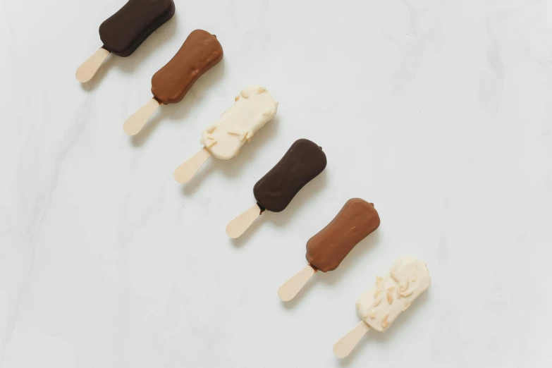 a row of ice cream pops sitting on top of a counter, by Nina Hamnett, hurufiyya, dark sienna and white, fully chocolate, 6 pack, spatula