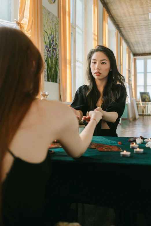 two women sitting at a table playing cards, by Julia Pishtar, pexels contest winner, hyperrealism, casting a protection spell, young asian woman, she is wearing a black tank top, wearing a luxurious silk robe