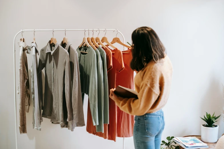 a woman standing in front of a rack of clothes, by Nicolette Macnamara, trending on pexels, wearing a linen shirt, presenting wares, for a catalogue, on a canva