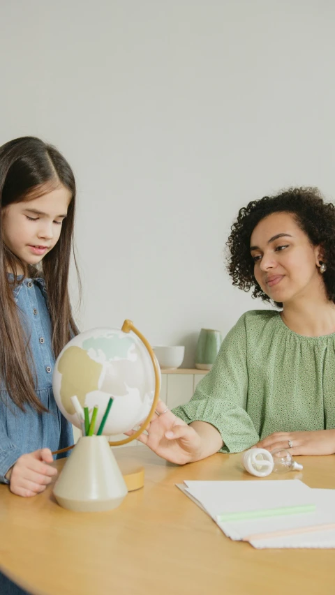 two women sitting at a table looking at a globe, a child's drawing, pexels contest winner, teacher, low quality photo, figurines, inspect in inventory image