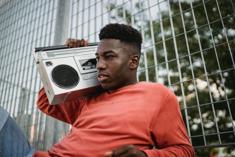 a man sitting in front of a fence holding a boombox, trending on pexels, man is with black skin, rectangle, male teenager, radio