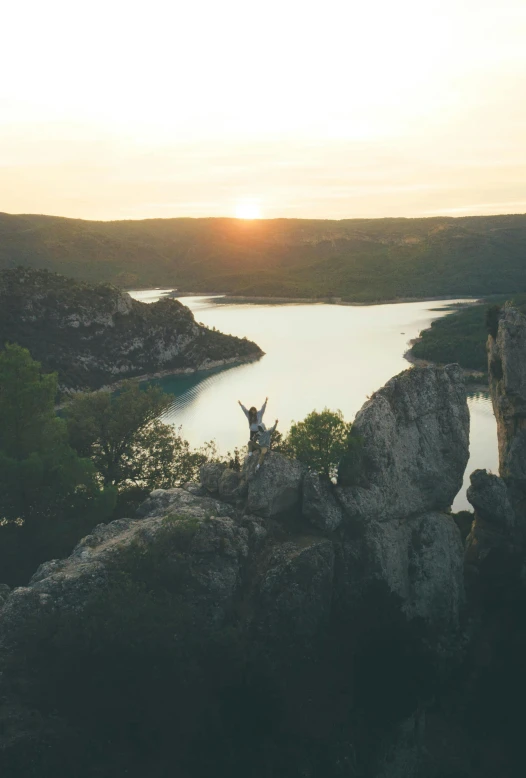 a person standing on top of a mountain next to a lake, during a sunset, over a calanque, mid air shot, instagram post