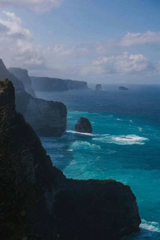 a group of people standing on top of a cliff next to the ocean, lush valley, deep azure tones, marsden, tall spires