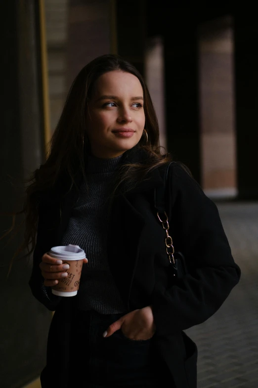 a woman standing on a sidewalk holding a cup of coffee, a portrait, inspired by Sydney Carline, pexels contest winner, renaissance, black jacket, portrait sophie mudd, 8k 50mm iso 10, 🤤 girl portrait