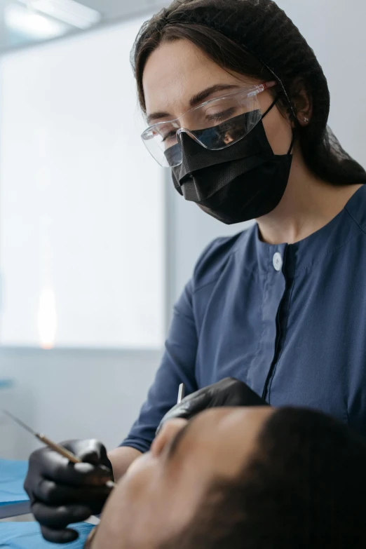 a woman getting her teeth examined by a dentist, a picture, shutterstock, wearing all black mempo mask, looking serious, carving, low quality photo