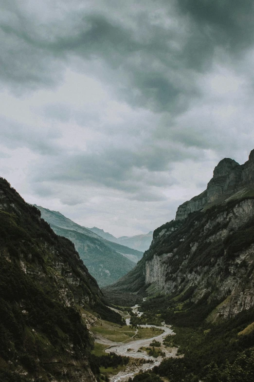 a river running through a valley surrounded by mountains, by Johannes Voss, pexels contest winner, visual art, dark towering clouds, lauterbrunnen valley, low quality footage, road between hills