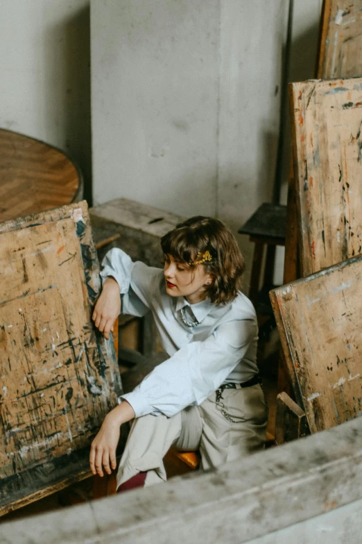 a man sitting on top of a wooden chair, inspired by Juan Luna, trending on unsplash, visual art, portrait androgynous girl, in a warehouse, leaning on door, thrown tables