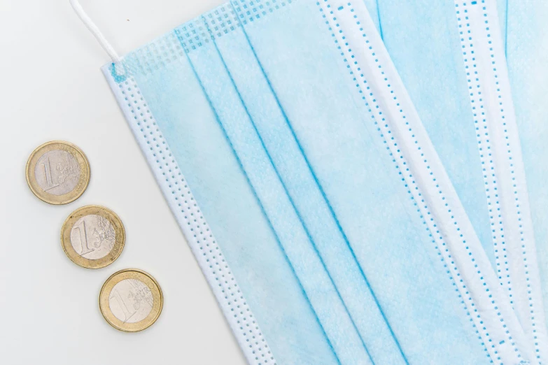 a blue face mask sitting on top of a pile of coins, trending on pexels, plasticien, banner, flat lay, pastel blue, view from the side