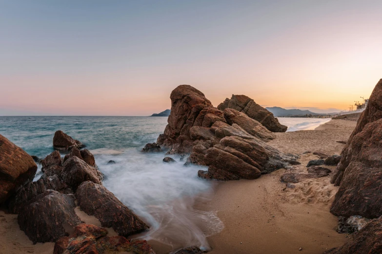 a large body of water sitting on top of a sandy beach, by Carlo Martini, unsplash contest winner, big rocks, sunset panorama, medium format. soft light, mountains and ocean