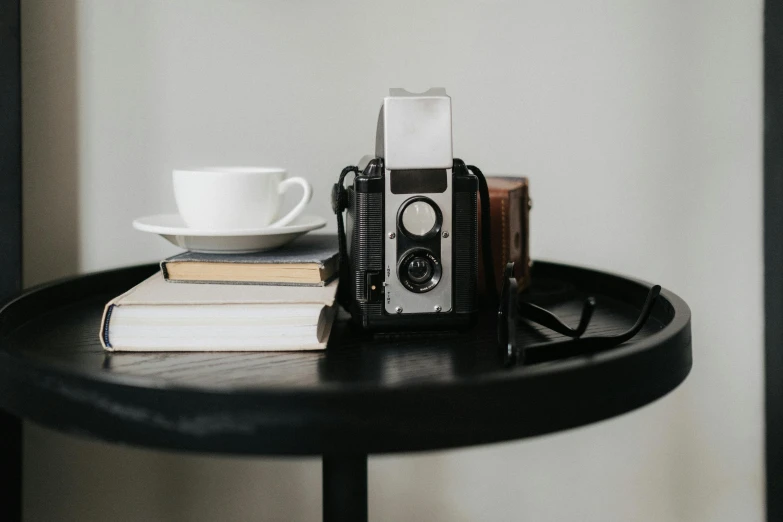 a camera sitting on top of a table next to a cup of coffee, stack of books on side table, rolleiflex, portait image, medium format