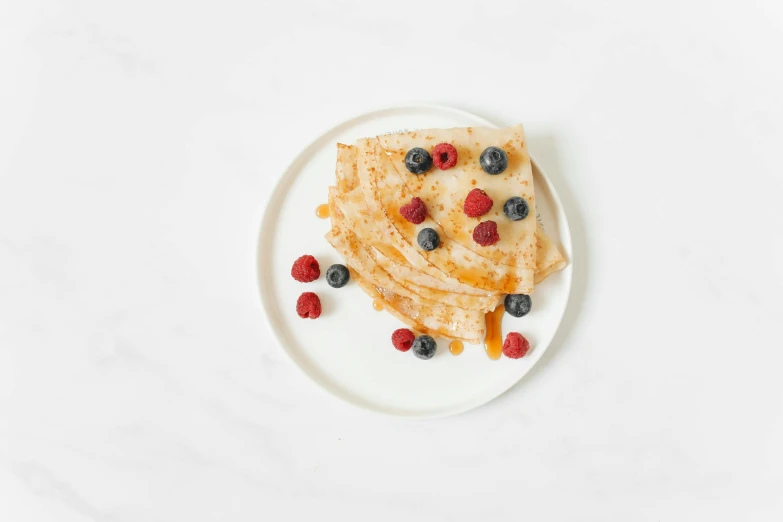 a white plate topped with pancakes and berries, unsplash, miniature product photo, folded, background image, birch