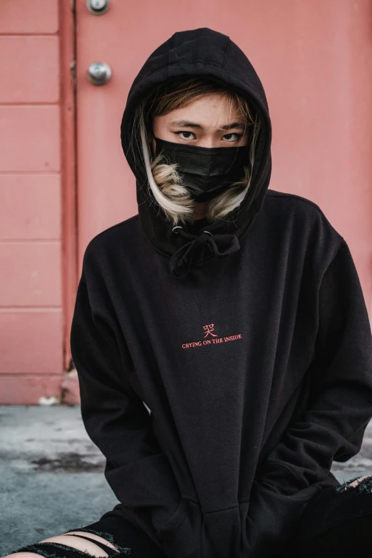 a woman sitting on the ground wearing a black hoodie, inspired by Zhu Da, trending on unsplash, masked face, official store photo, wearing a baggy, slight color bleed