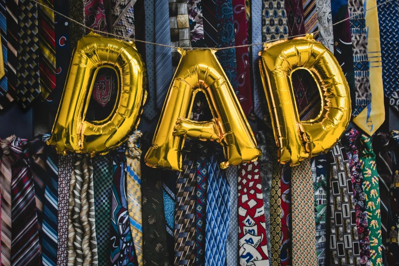 a gold balloon shaped like the word dad hanging from a line of ties, a cartoon, by Julia Pishtar, pexels, dada, patterned scarf, a handsome, te pae, official